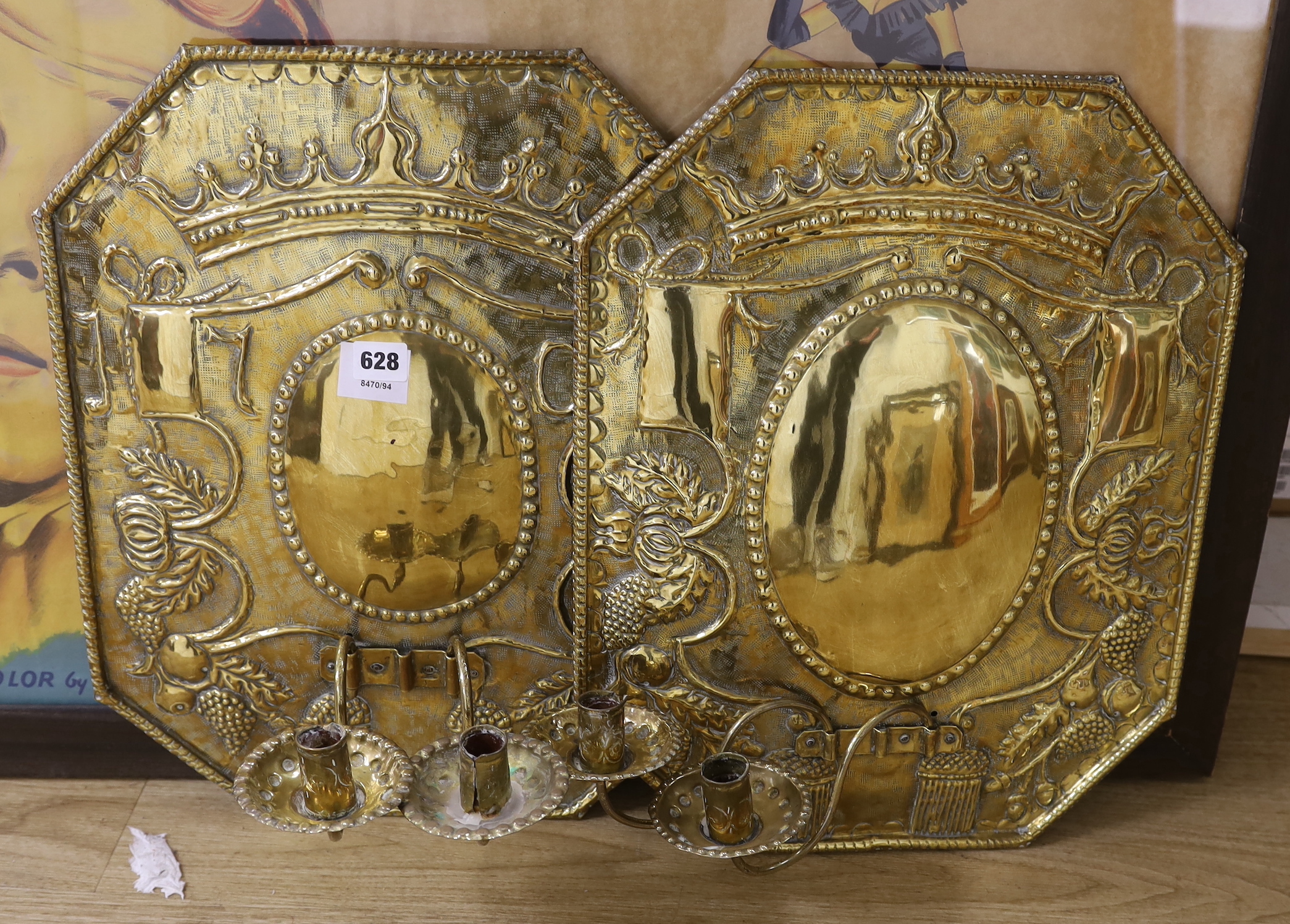 A pair of brass wall sconces, each with embossed reflector backplates supporting two branches, one inscribed 1705